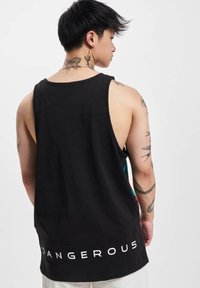Svart singlet laget av bomull, med en stor hvit "DANGEROUS" trykk på kanten og en avslappet passform med brede armhull.
