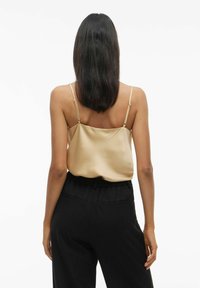 Satiinist, õlavaba, beež ülemine osa, millel on reguleeritavad rihmad, kantud mustade kõrge vöökohaga pükstega, millel on küljetaskud ja lõdva lõikega.