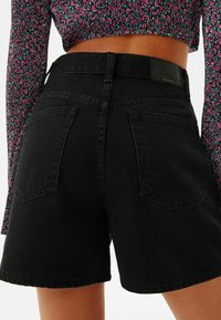 Svarta denimshorts har hög midja, två bakfickor och en märkesetikett. Texturen verkar robust, med en snygg finish vid kanterna.