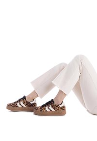 Zapatillas con estampado de leopardo y cordones negros, rayas blancas y una suela de goma color beige. Combinadas con unos pantalones cortos de color crema.