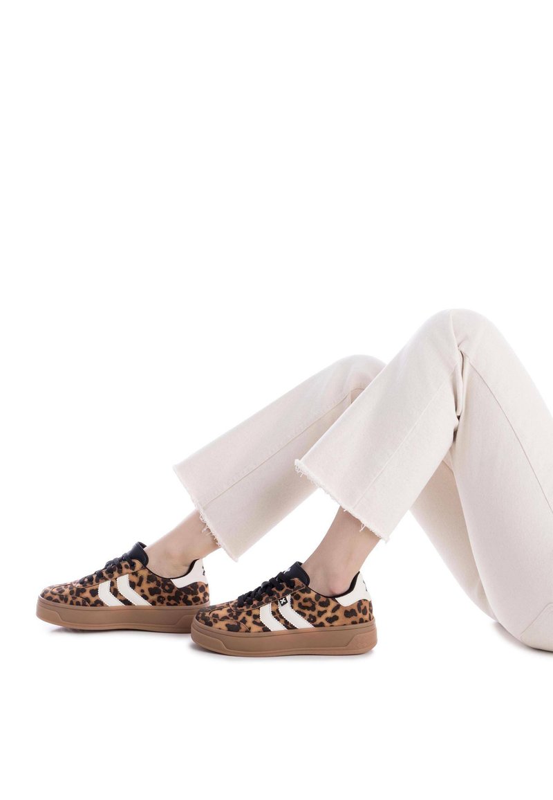 Zapatillas con estampado de leopardo y cordones negros, rayas blancas y una suela de goma color beige. Combinadas con unos pantalones cortos de color crema.