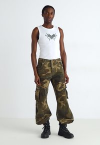 Canotta bianca con un design grafico, abbinata a pantaloni cargo mimetici oversize e stivali neri con lacci. Tessuto morbido, vestibilità ampia.