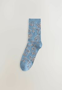 Ljusblå ankelsocka med ett upprepat mönster av konturerade hundar i beige och brunt, med en mjuk, stickad textur.