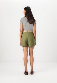 Shorts vert olive à coupe droite, associés à un haut à manches courtes noir et blanc à rayures, avec une ceinture tissée et deux poches arrière.