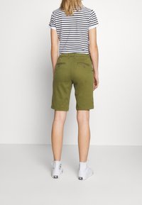 Vihreät puuvillahousushortsit, joissa käännetyt reunat ja kaksi takataskua, joissa on nappiyksityiskohdat, yhdistetty raitapaitaan, jossa on lyhyet hihat, ja valkoisiin tennareihin.