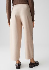 Beige wijde broek met een tailored fit, voorzien van achterzakken en een gladde textuur, gecombineerd met bruine schoenen.