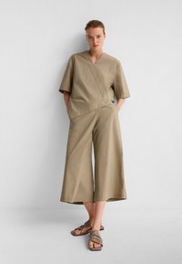 Top avvolgente beige con maniche corte, abbinato a pantaloni larghi in un tessuto coordinato. Sandali testurizzati completano il look.