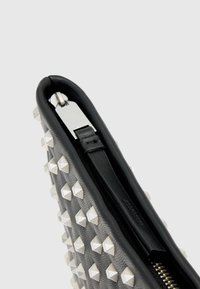 Czarna teksturowana skórzana saszetka z ozdobami z srebrnych ćwieków i zamkiem błyskawicznym, z gładkim, wewnętrznym wyściełaniem oraz srebrnymi elementami metalowymi.