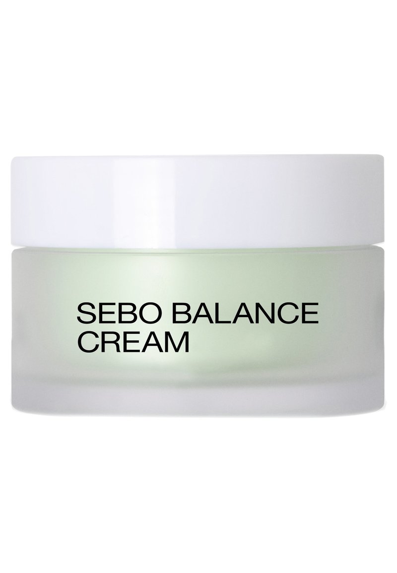 Crème Sebo Balance dans un pot en verre givré avec un couvercle blanc ; crème verdâtre visible à l'intérieur ; texte noir en gros sur l'étiquette avant.