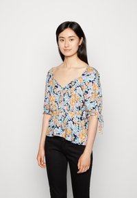 Blusa floral em azul-marinho escuro com flores laranja e azul claro, mangas curtas com volume, decote em V e cintura ajustada. Combinada com calças pretas.