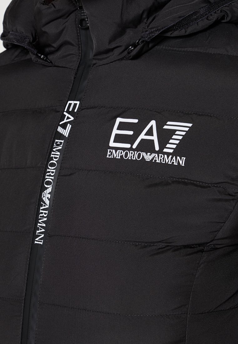 Czarna, ocieplana kurtka z zapięciem na zamek. Posiada kaptur i białe logo "EA7 Emporio Armani". Gładka tekstura z pikowanymi sekcjami.
