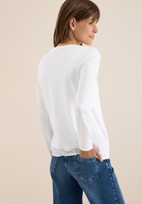 Langärmliges weißes T-Shirt aus weicher Baumwolle, mit rundem Halsausschnitt und bequemen Schnitt, kombiniert mit mitteldunkelblauen Jeans.