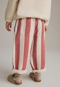Pantalons en coton rayés rouges et crème, avec poches plaquées, ourlets roulés et coupe décontractée, associés à des sabots beiges et des chaussettes à côtes.