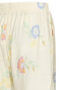 Pantalon couleur crème avec une ceinture élastique ornée d'un motif floral pastel brodé en points de croix dans des nuances de bleu, jaune, rose et vert.