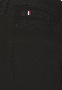 Jeans de mezclilla negra con un pequeño logo tricolor en el bolsillo trasero, con una textura suave y un diseño ajustado.