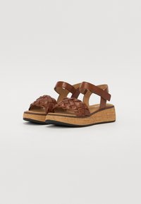 Sandali wedge in pelle marrone con una fascia intrecciata sulla punta, cinturino alla caviglia regolabile e suola in sughero. Texture liscia e design minimalista.