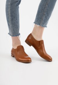 Bruine leren instapschoenen met een gladde afwerking, ronde neuzen en lage blokhakken, gecombineerd met blauwe jeans met een verouderde zoom.