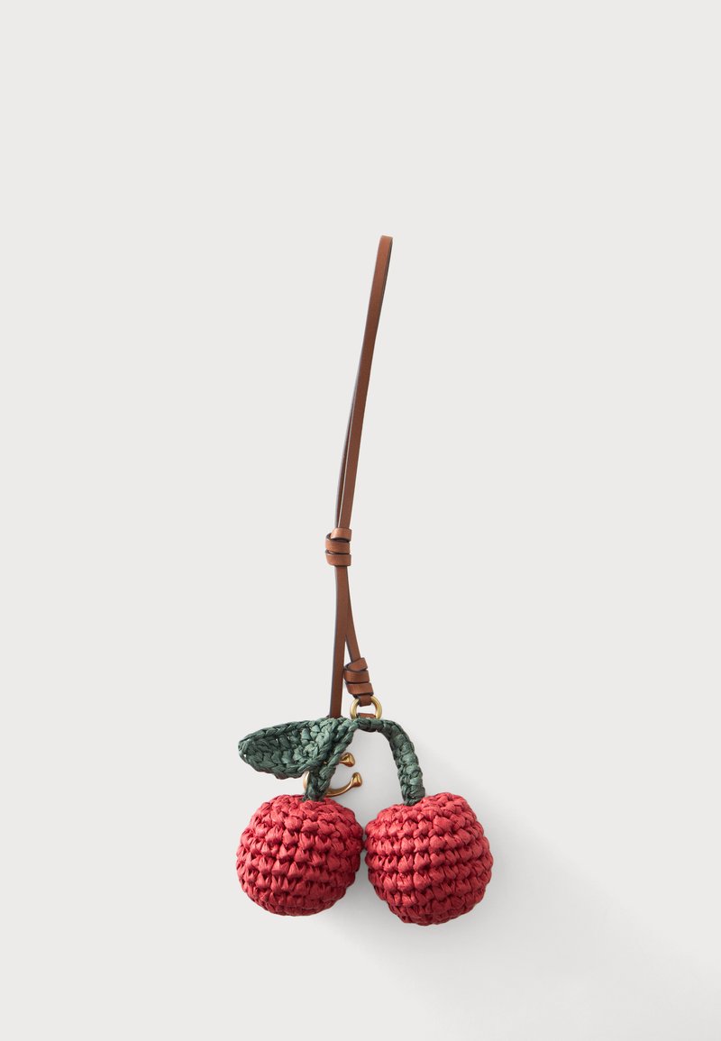 Porte-clés avec deux cerises rouges au crochet et une feuille verte attachée à une lanière en cuir marron en boucle sur fond blanc.