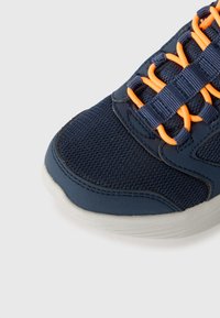 Baskets bleu marine avec lacets élastiques oranges, tige en mesh et semelle blanche, présentées en gros plan sur un fond blanc.