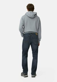 Grijze hoodie en donkerblauwe spijkerbroek. De hoodie heeft een ruime capuchon en de spijkerbroek heeft een klassiek vijf-pocket ontwerp met stiksel details.