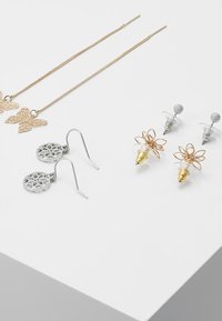 Gula fjärilspendante öronhängen, silverblommiga utskurna öronhängen, guld- och silverblommor studörhängen, samt en strukturerad kristallstudörhänge.