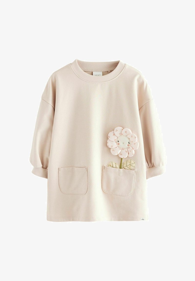 Sweatshirt rose clair coupe oversize, manches courtes bouffantes, deux poches avant et un motif appliqué de fleur sur la poche gauche.