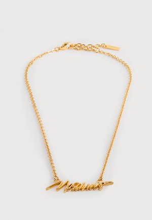 Collier doré avec un pendentif en forme de plaque nominative cursive, doté d'une chaîne délicate et d'un fermoir mousqueton.