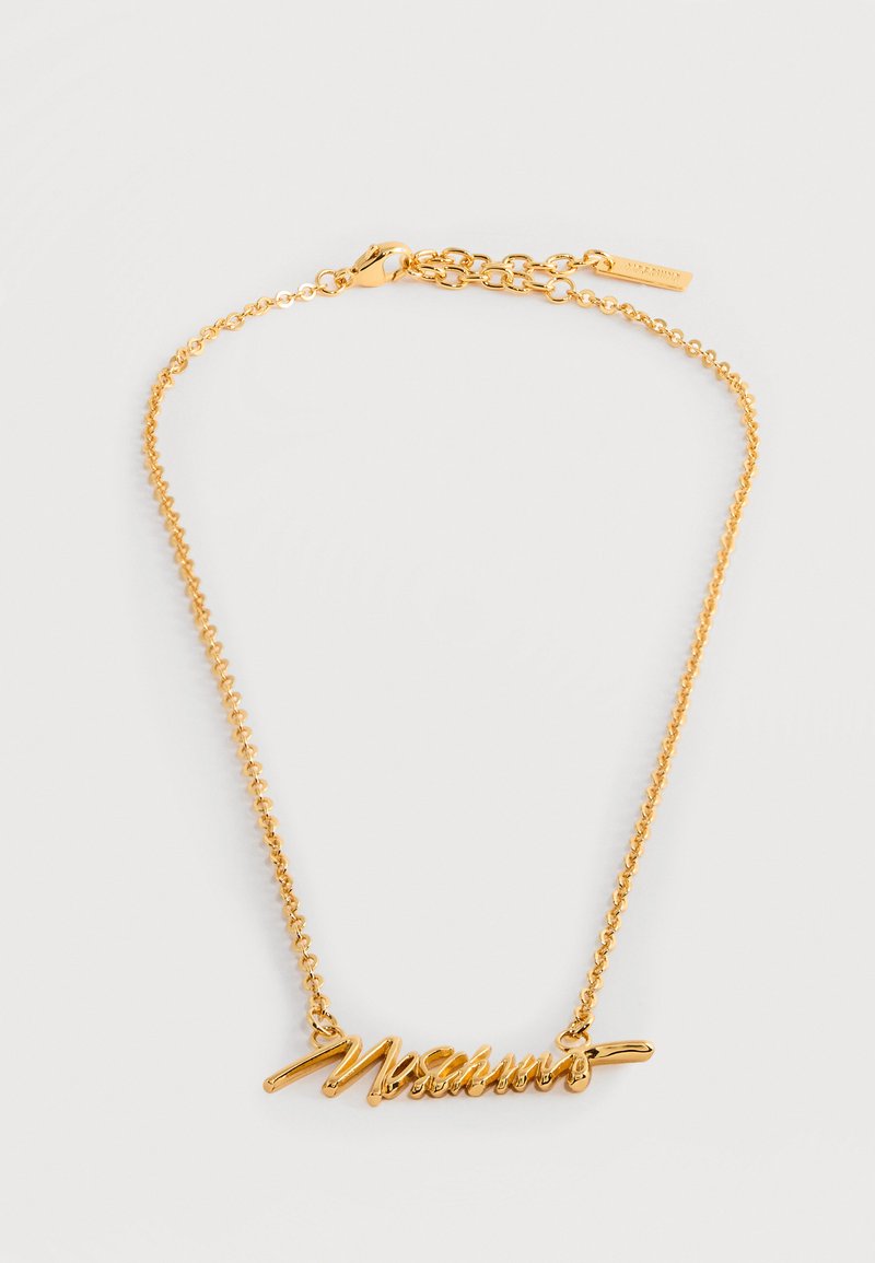 Auksu tone dažytas vėrinys su rašytinio stiliaus vardinio pakabuko motyvu, subtilia grandinėle ir užsegimu omaro formos sagtimi.