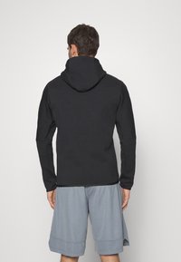 Felpa nera con cappuccio dal tessuto morbido, maniche lunghe e vestibilità rilassata, abbinata a pantaloni sportivi grigi chiari.