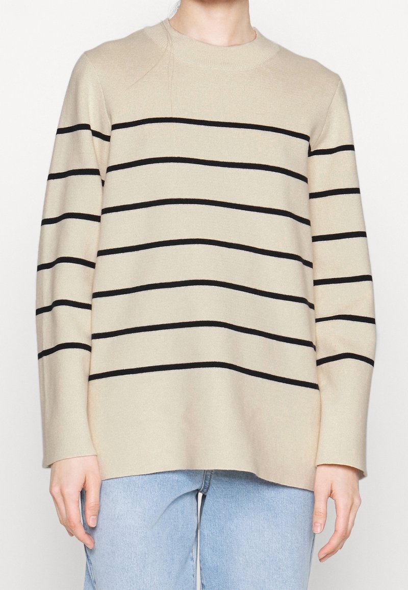 Beige gebreide trui met zwarte horizontale strepen, ronde hals, lange mouwen, een relaxte pasvorm en een zachte textuur, gecombineerd met lichtblauwe denim.