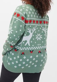 Hellgrüner Pullover mit weißen Rentieren, roten Herzen und geometrischen Mustern. Verfügt über einen gerippten Ausschnitt und Saum. Weiche Stricktextur.