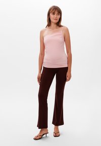Světle růžový top na jedno rameno ze strečového materiálu; spárován s tmavě hnědými rozšířenými kalhotami. Modelka má na sobě hnědé sandály na pásku a stojí na jednobarevném pozadí.