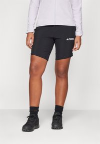 Schwarze Sportshorts mit einem eng anliegenden Design. Sie bestehen aus elastischem Gewebe und verfügen über ein weißes "TERREX"-Logo am linken Oberschenkel.