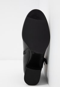 Semelle de chaussure en cuir noir avec bande de roulement texturée, petit talon, taille 37 visible, positionnée verticalement sur fond blanc.