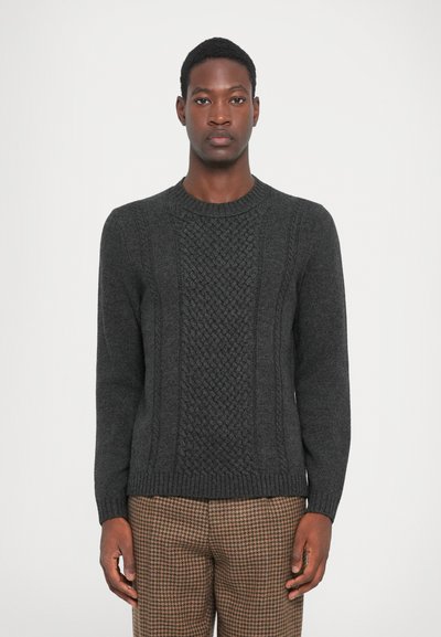 Dunkelgrauer Strickpullover mit strukturiertem Mittelteil und geripptem Ausschnitt. Lange Ärmel und figurbetonter Saum, getragen mit karierter brauner Hose.