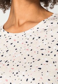 Světle béžové tričko s kulatým výstřihem, s tečkovaným vzorem v růžové, černé, bílé a žluté barvě, vyrobené z měkké tkaniny.