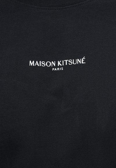 Μαύρο ύφασμα με λευκό κείμενο «MAISON KITSUNÉ» πάνω από μικρότερο «PARIS» στο κέντρο της άνω περιοχής του στήθους ενός ρούχου.
