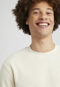 Pull à col rond texturé de couleur claire, avec un col côtelé, présentant un motif subtil et une coupe décontractée.