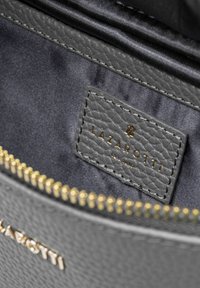 Graues strukturiertes Lederinnere der Tasche mit einem goldenen Reißverschluss, einem dunklen Stofffutter und einem grauen Etikett, das mit "LAZAROTTI" geprägt ist.