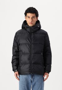 Chaqueta acolchada negra con textura de acolchado, cuello alto con capucha, cierre de cremallera y bolsillos laterales. Diseñada con un mínimo de detalles metálicos.