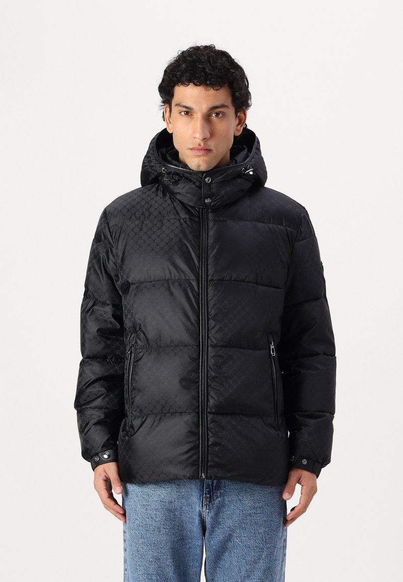 Giacca nera imbottita con texture trapuntata, colletto alto con cappuccio, chiusura con zip e tasche laterali. Progettata con minimalismi negli accessori metallici.