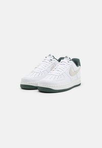 Bílé sportovní boty s texturovaným svrškem, zelenou gumovou podrážkou a béžovým designem swoosh. Mezi vlastnostmi je perforace pro prodyšnost.