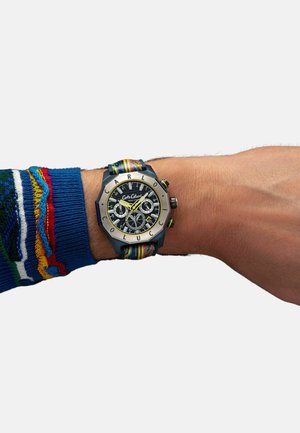 Mehrfarbige Stoffarmbanduhr mit schwarzem Zifferblatt, silbernen Akzenten und kräftigen gelben Stundenmarkierungen auf einem sechseckigen Metallgehäuse.