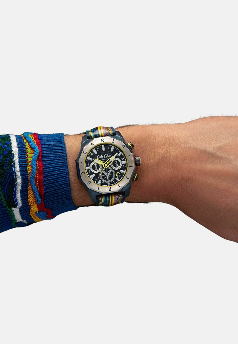 Orologio con cinturino in tessuto multicolore, caratterizzato da un quadrante nero, inserti argento e audaci indicatori delle ore gialli su una cassa metallica esagonale.