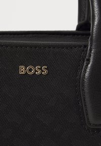 Black handbag featuring a textured surface, gold embossed "BOSS" logo, and smooth leather accents. Square shape with short handles.