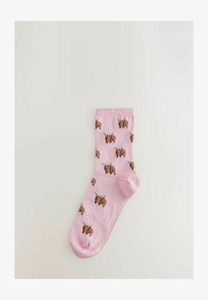 Lyserøde sokker med et gentaget mønster af brune dyr med lysere accenter. Fremstillet af et glat, strækbart materiale.