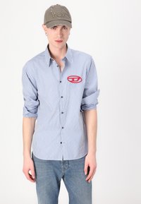 Blue and white striped shirt with a red embroidered logo on the left chest, paired with a gray cap featuring the word "Won."