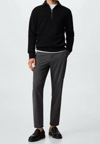 Pull noir zippé, pantalon gris ajusté et mocassins noirs. Tissu lisse, coupe slim et design minimaliste sans motifs visibles.