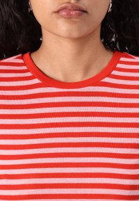 Rød og rosa stripete t-skjorte med ribbet rund hals. Stoffet ser mykt og tettsittende ut, med jevnt fordelte horisontale striper.