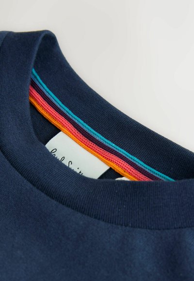 Suéter azul marino con cuello redondo, ribete a rayas de colores en el interior del cuello y una etiqueta blanca de prenda parcialmente visible.